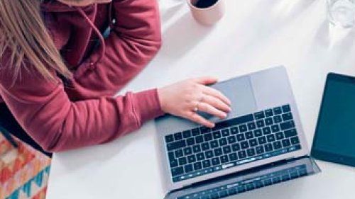 To unge kvinder sider ved et spisebord og kigger i rejsebøger og på en computer