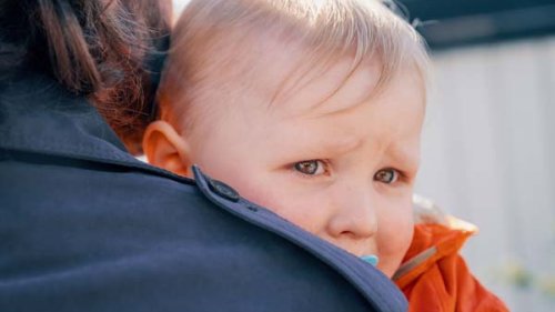 En lille dreng med sut i munden og våde øjne trøstes på skulderen af en voksen.