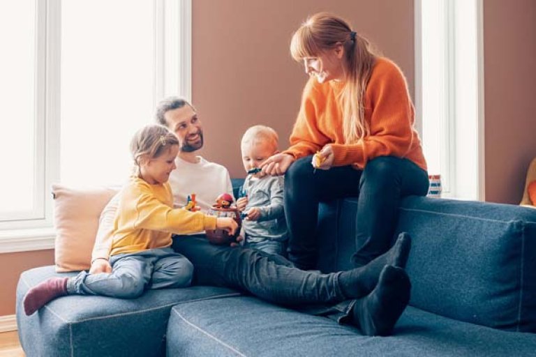 En familie bestående af mor, far og to børn sidder i sofaen i deres hjem