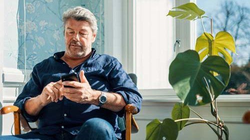 Ældre mand sidder i stol med telefon og skriver