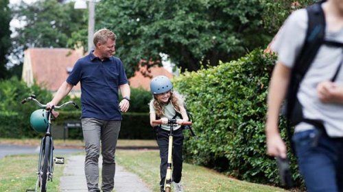 Far og datter går udenfor med cykel og løbehjul