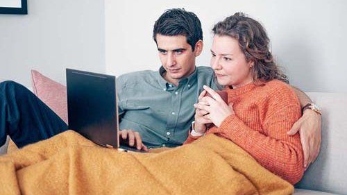 Par der ligger i sofaen og kigger på computeren