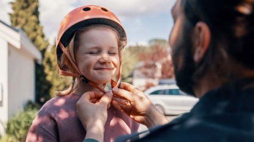 Pige får cykelhjelm på af far udenfor