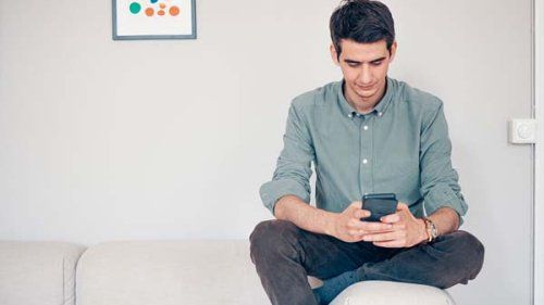 Mand sidder med sin mobil på en sofa